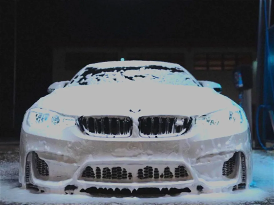 Witte BMW onder een dikke laag shampooschuim in een donkere wasbox