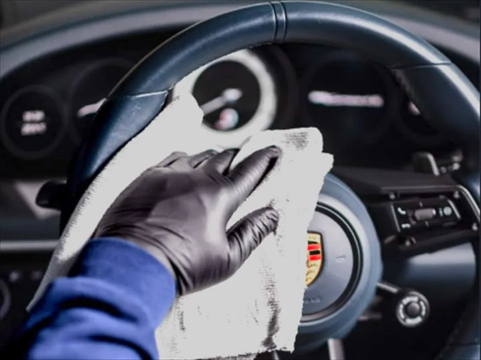 Zwarte handschoen met een microvezeldoek die het stuurwiel van een Porsche reinigt